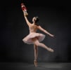 A ballerina en pointe in a pink tutu and crown holding up a wooden nutcraker