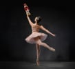 A ballerina en pointe in a pink tutu and crown holding up a wooden nutcracker
