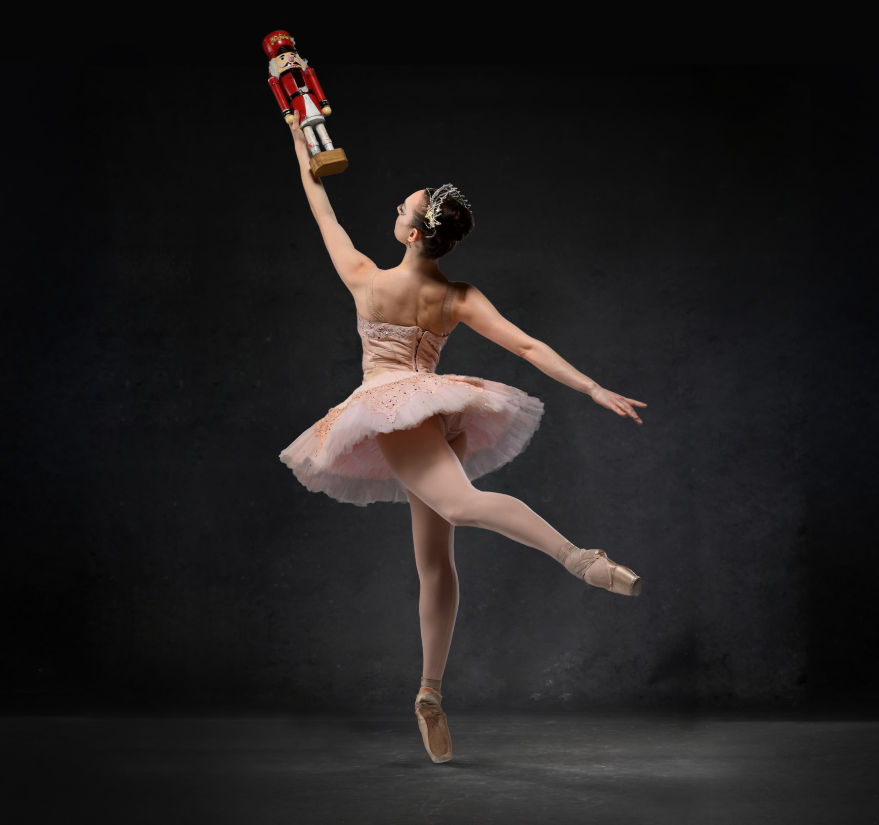 A ballerina en pointe in a pink tutu and crown holding up a wooden nutcraker