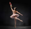 A ballerina in a pink tutu and crown poses en pointe holding up a wooden nutcracker