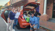 Photo of Committee Members standing beside a car full of food.