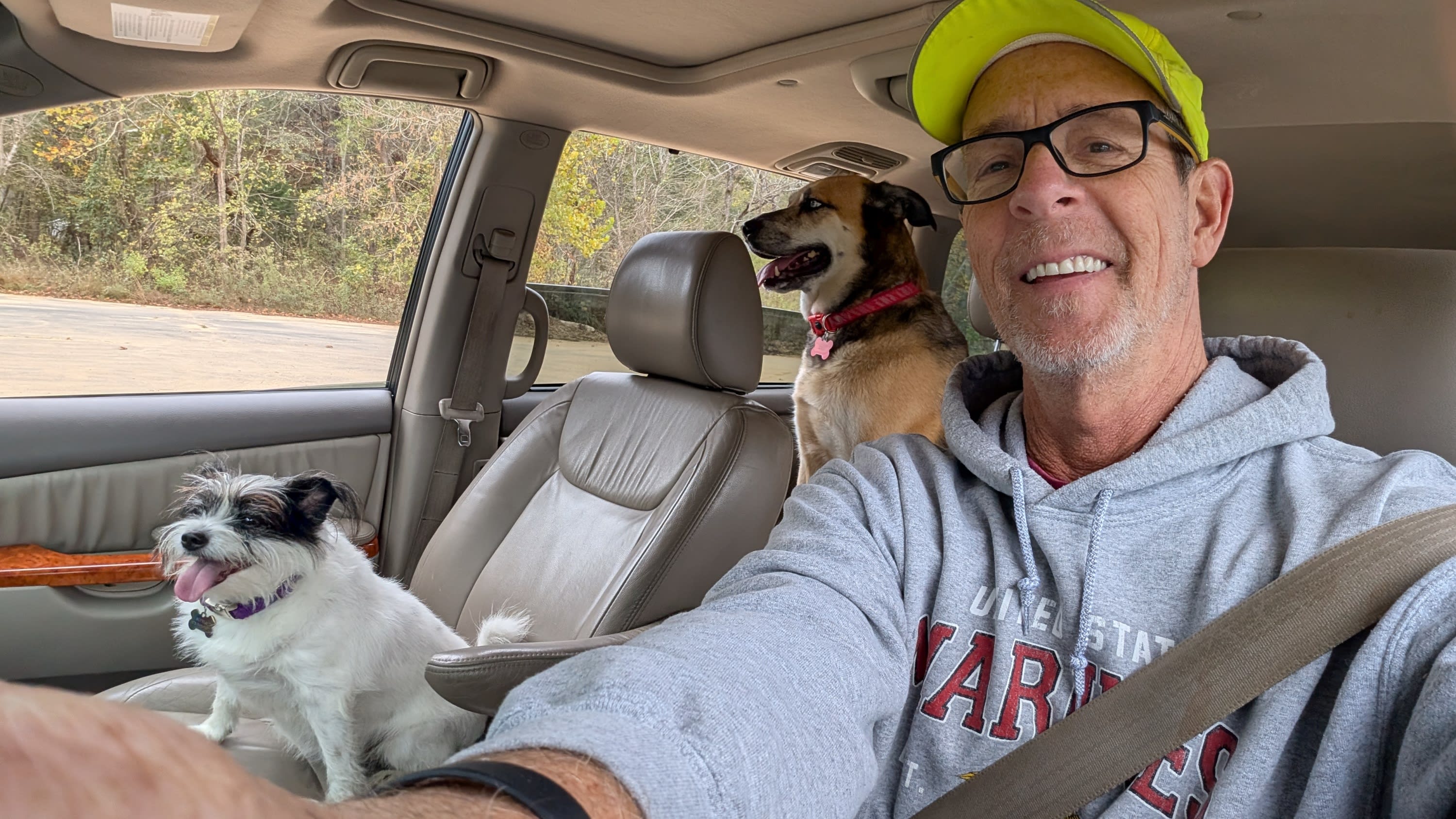 Two happy dogs with tongues out and a smiling man with a cap and glasses