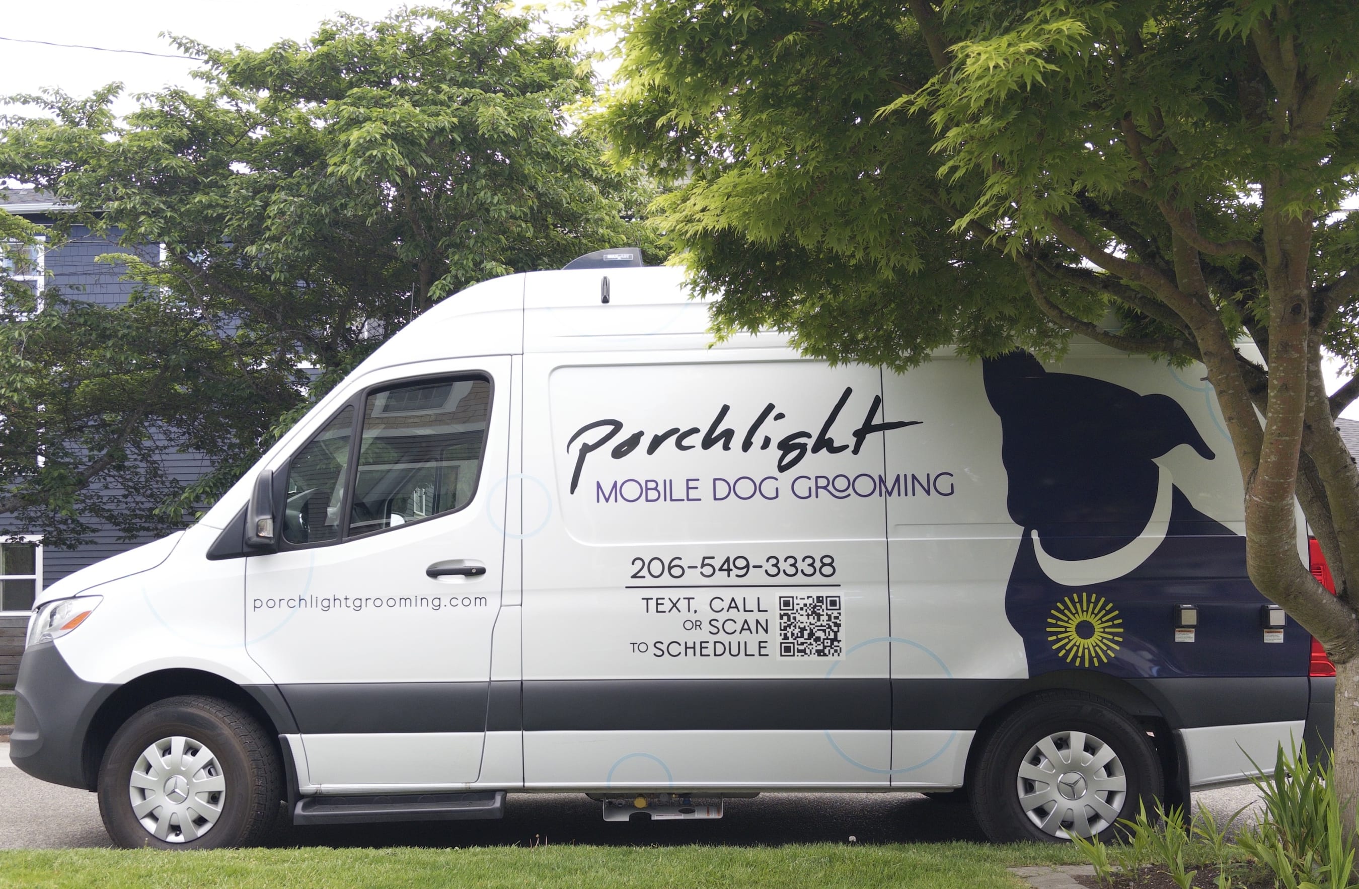 White Mercedes Sprinter van parked on a neighborhood street beneath a lush tree. Art on the van shows the Porchlight logo.