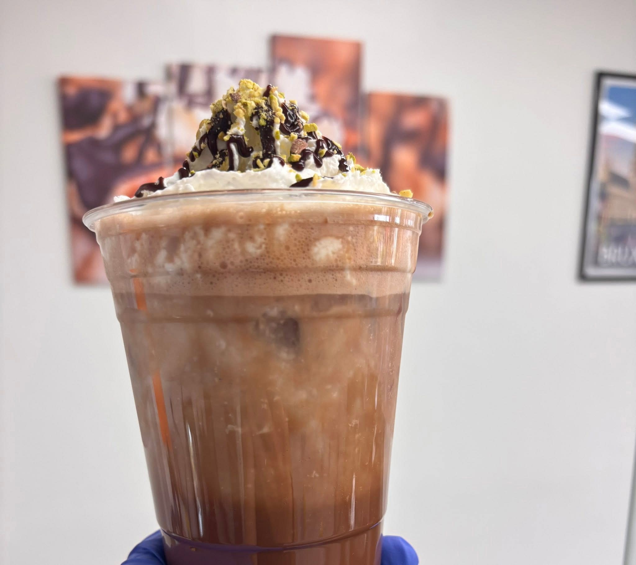 Close-up of an iced chocolate drink topped with whipped cream, chocolate drizzle, and crushed pistachios.
