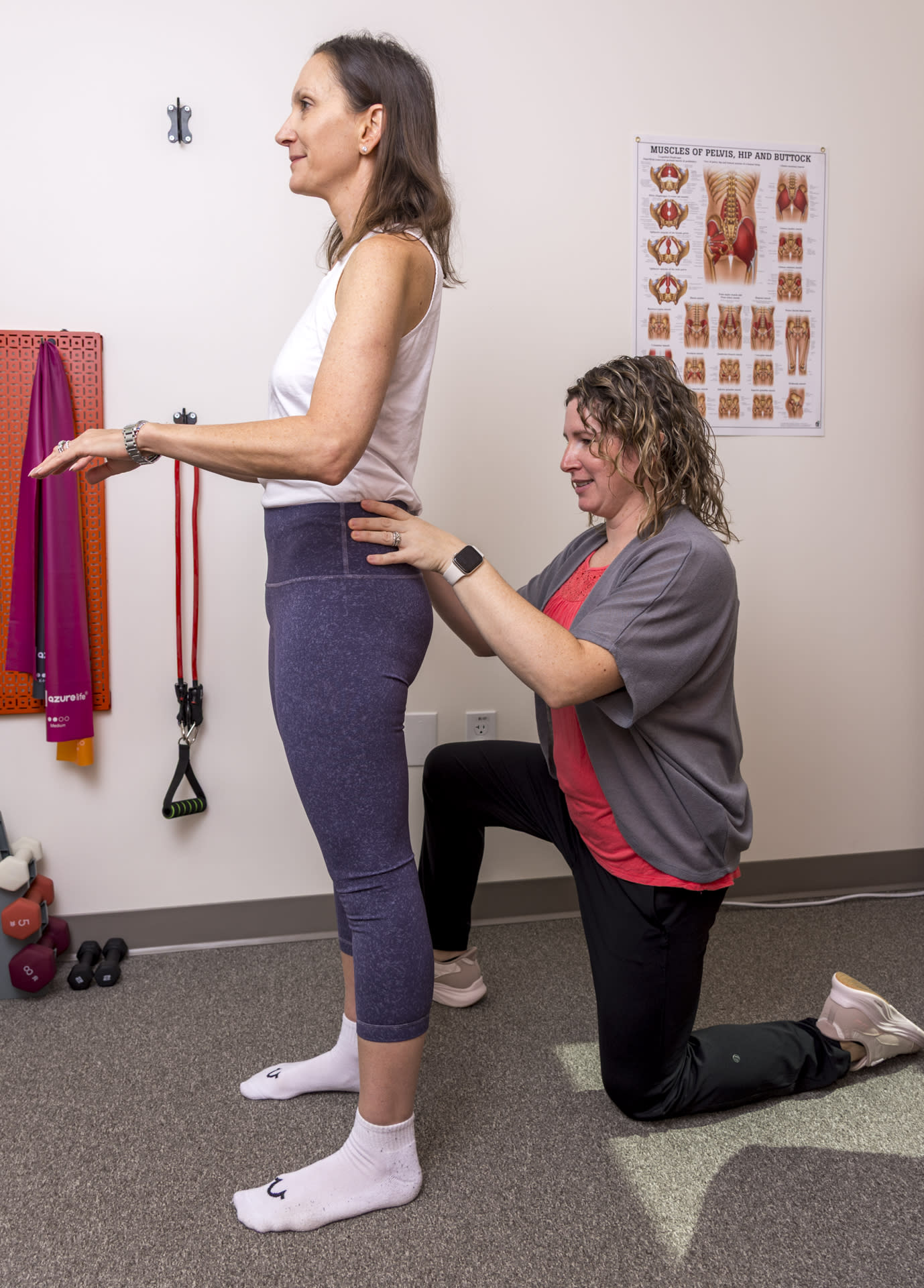 physical therapist touching a patient's lower back while standing to check pelvis