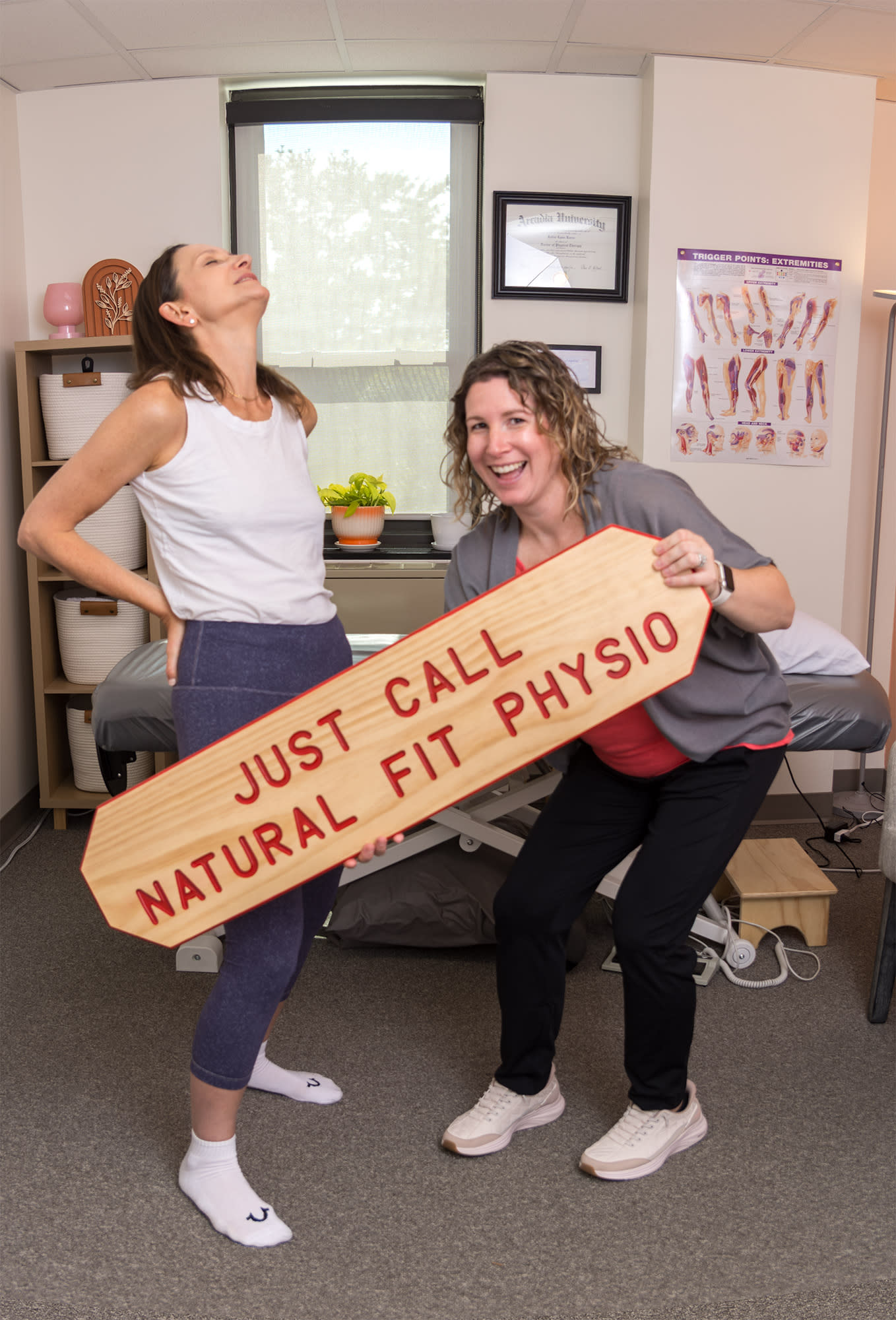 woman holding her back in pain and physical therapist holding sign that reads just call Natural Fit Physio