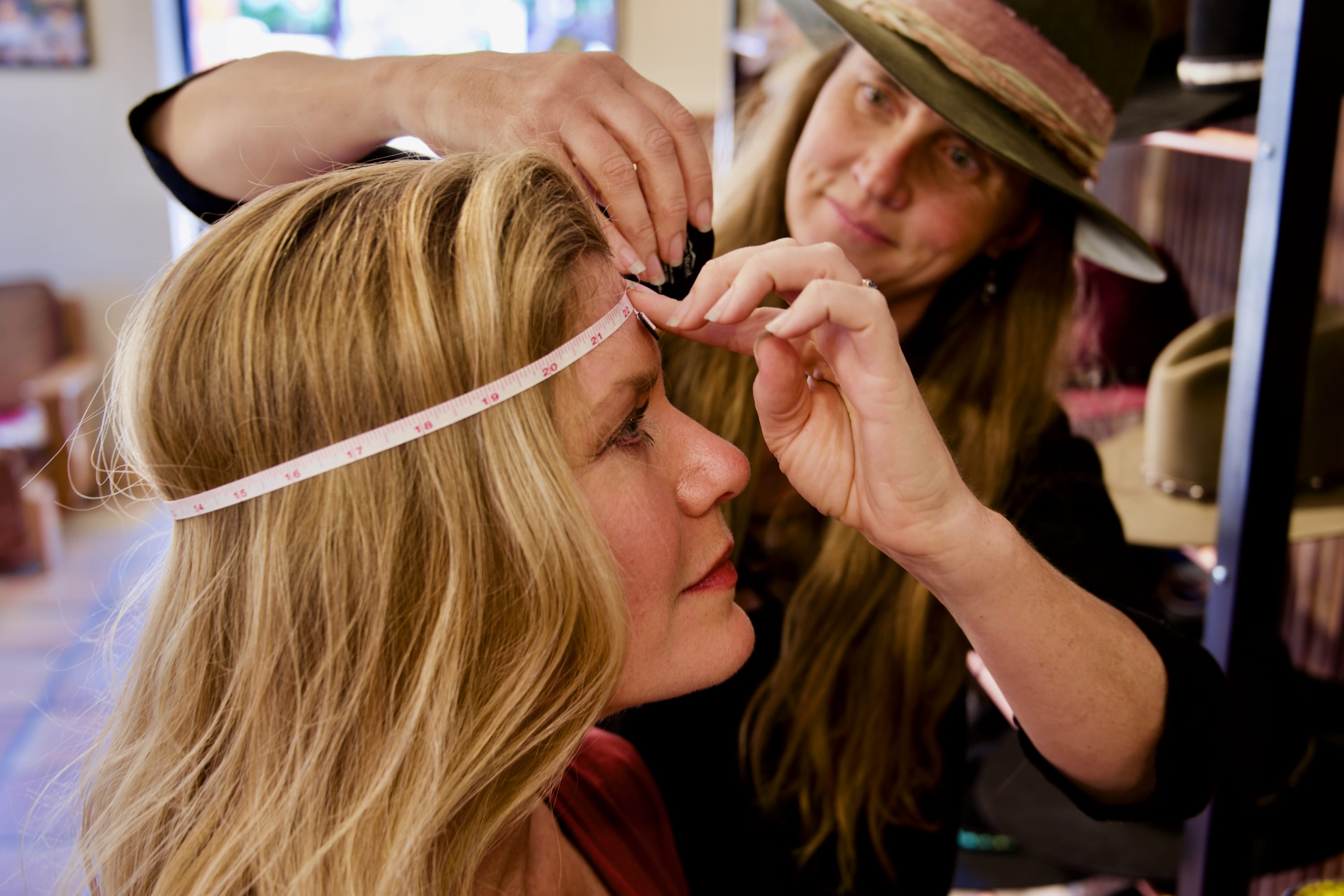 Woman helping another woman measure head for hat