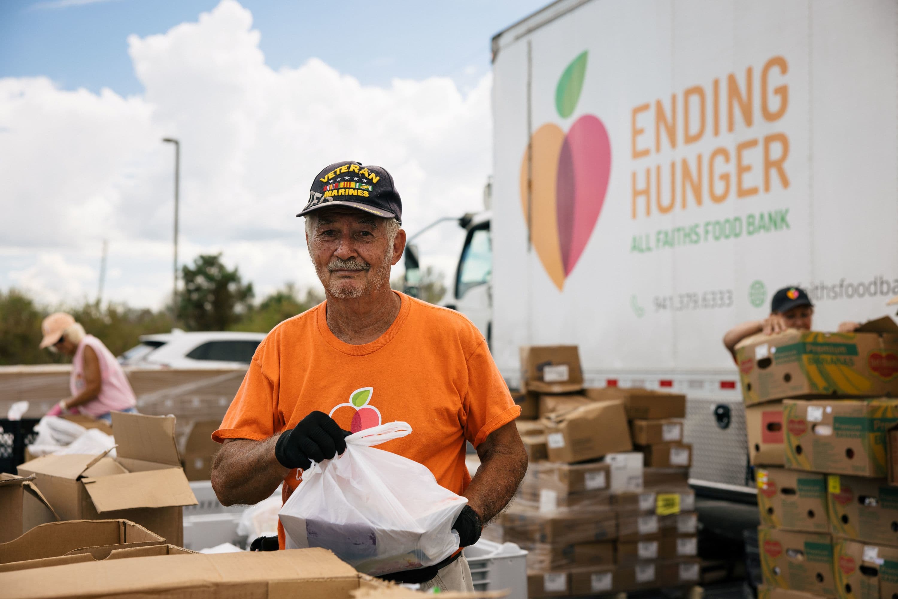 Veteran holding a package of food while volunteering with All Faiths Food Bank