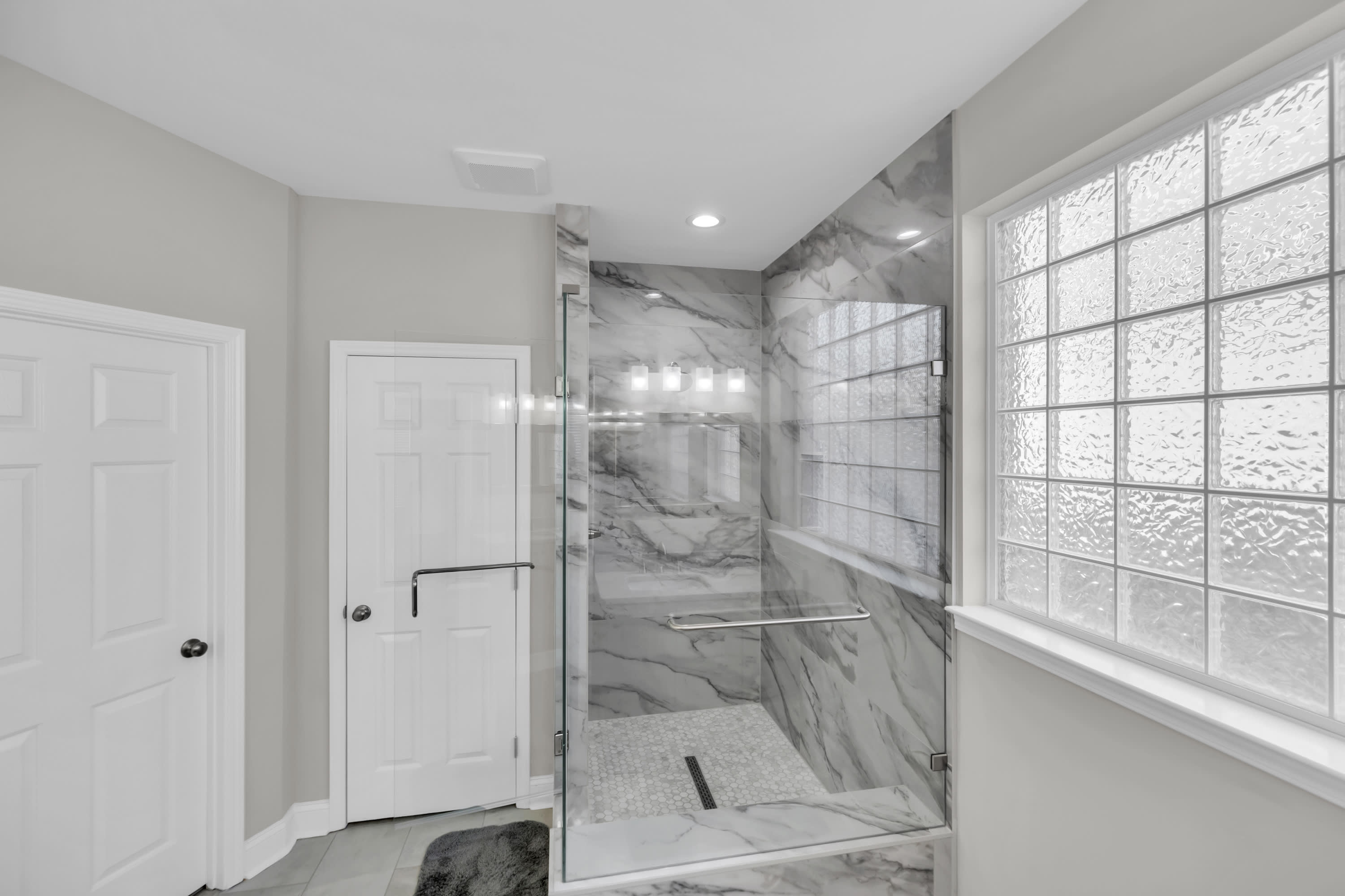 Custom walk in shower featuring marble look wall tile, frameless glass enclosure, built in bench, and natural light