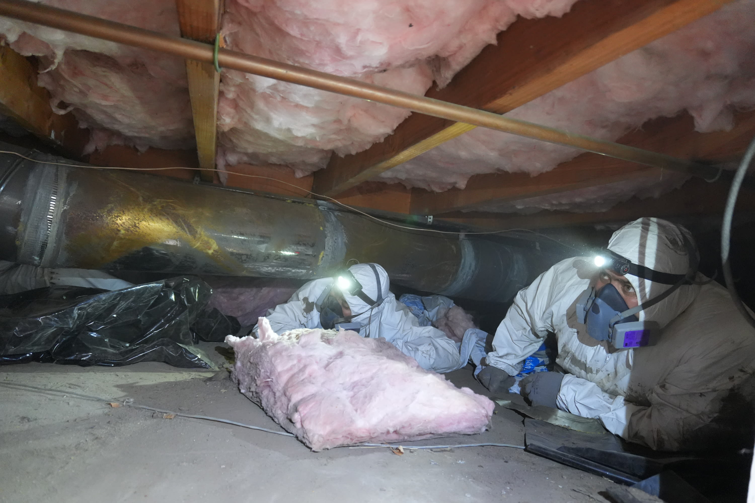 Technician installing insulation between floor joists in a crawl space to improve thermal efficiency.