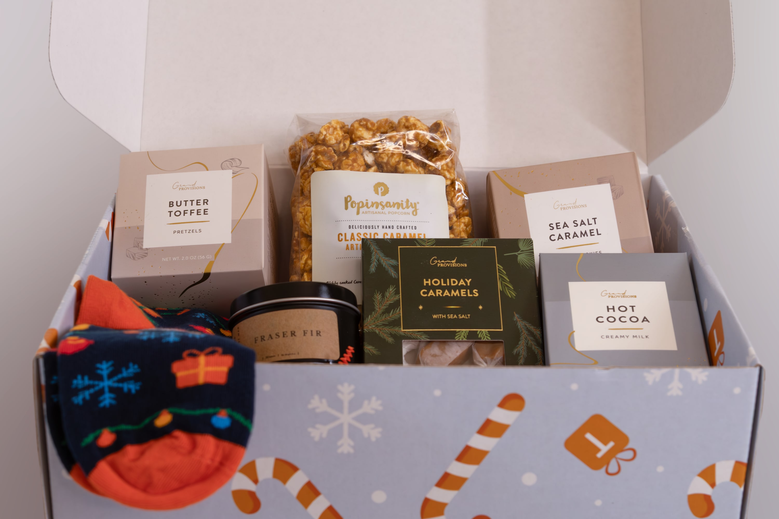 Corporate holiday gift box with branded packaging, festive socks, caramel popcorn, hot cocoa, and gourmet treats