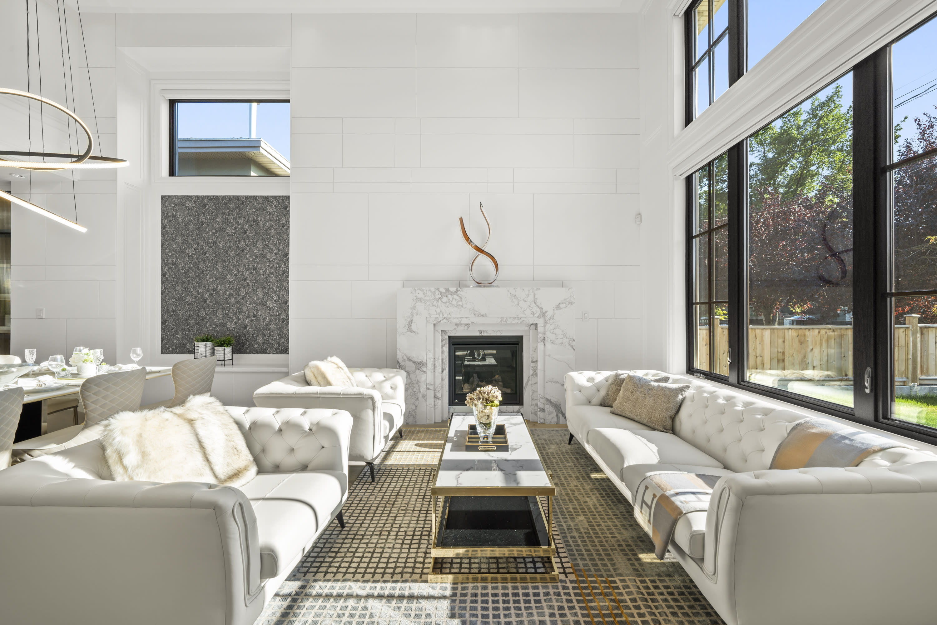 Luxury living room at 8080 Alanmore Place featuring double-height windows, a marble fireplace, custom wall detailing, modern