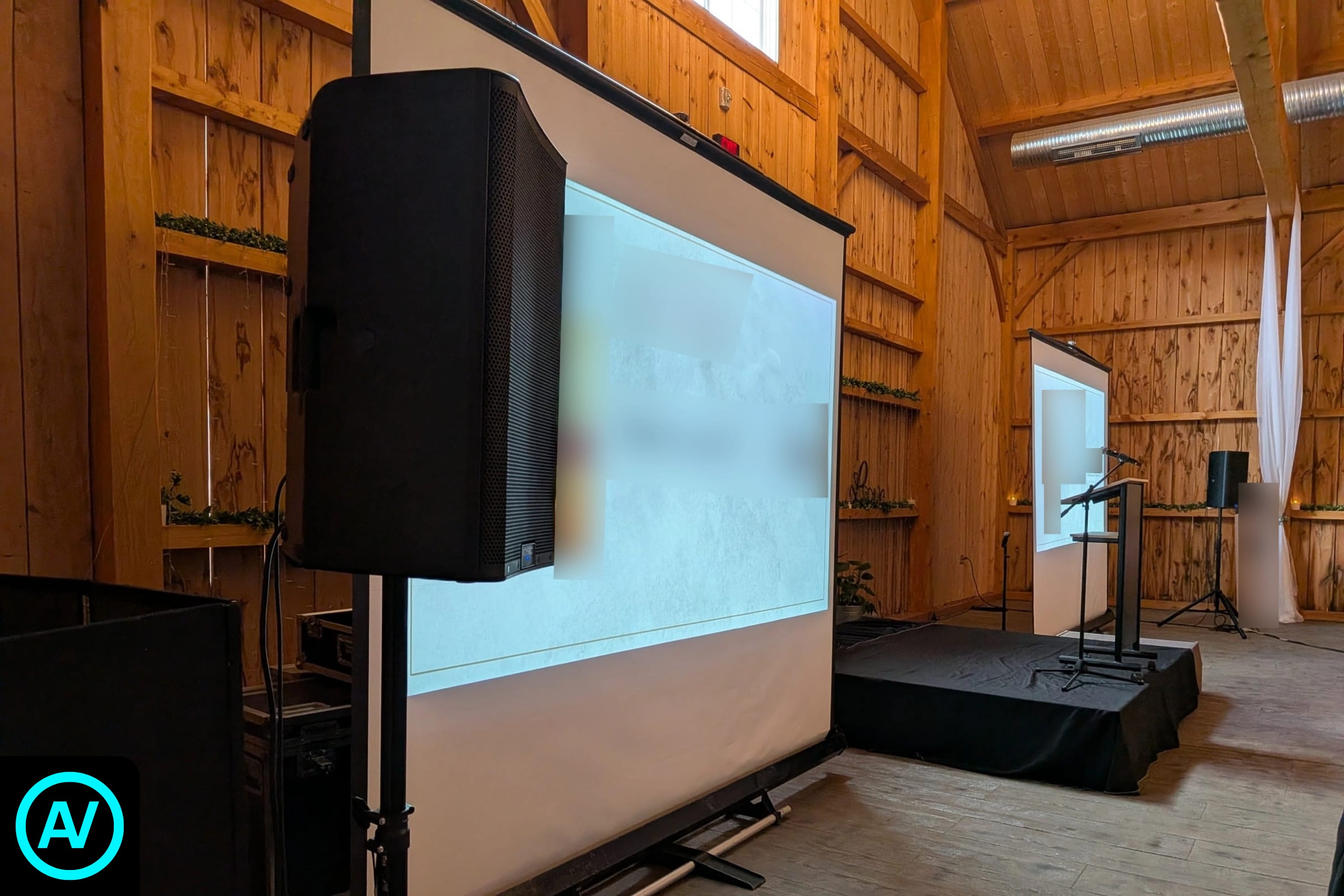 Dual projection screens, sound system, microphones, and podium arranged inside a rustic event venue