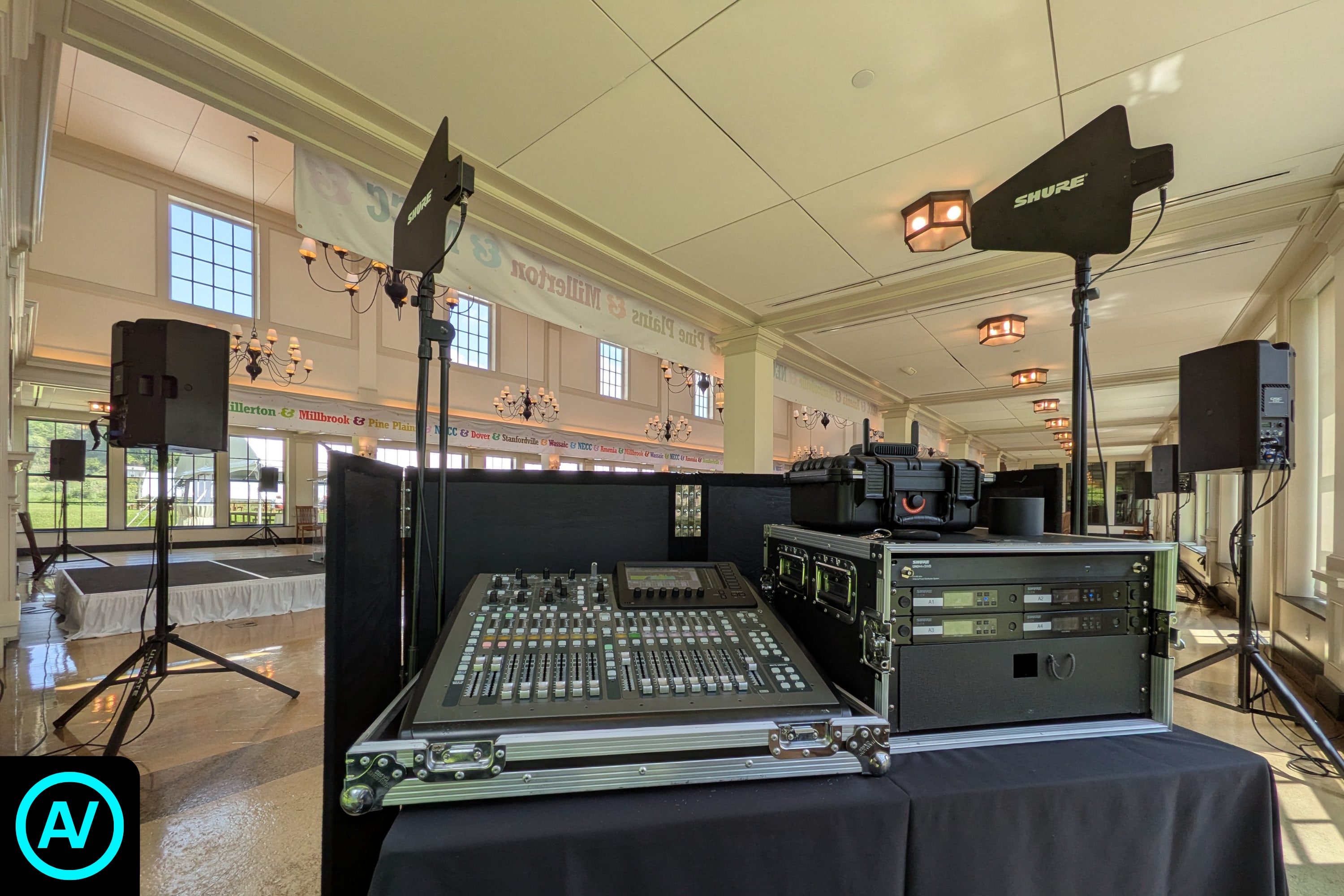 Digital audio mixing console, wireless microphone system, antennas, and speakers set up inside a large event hall