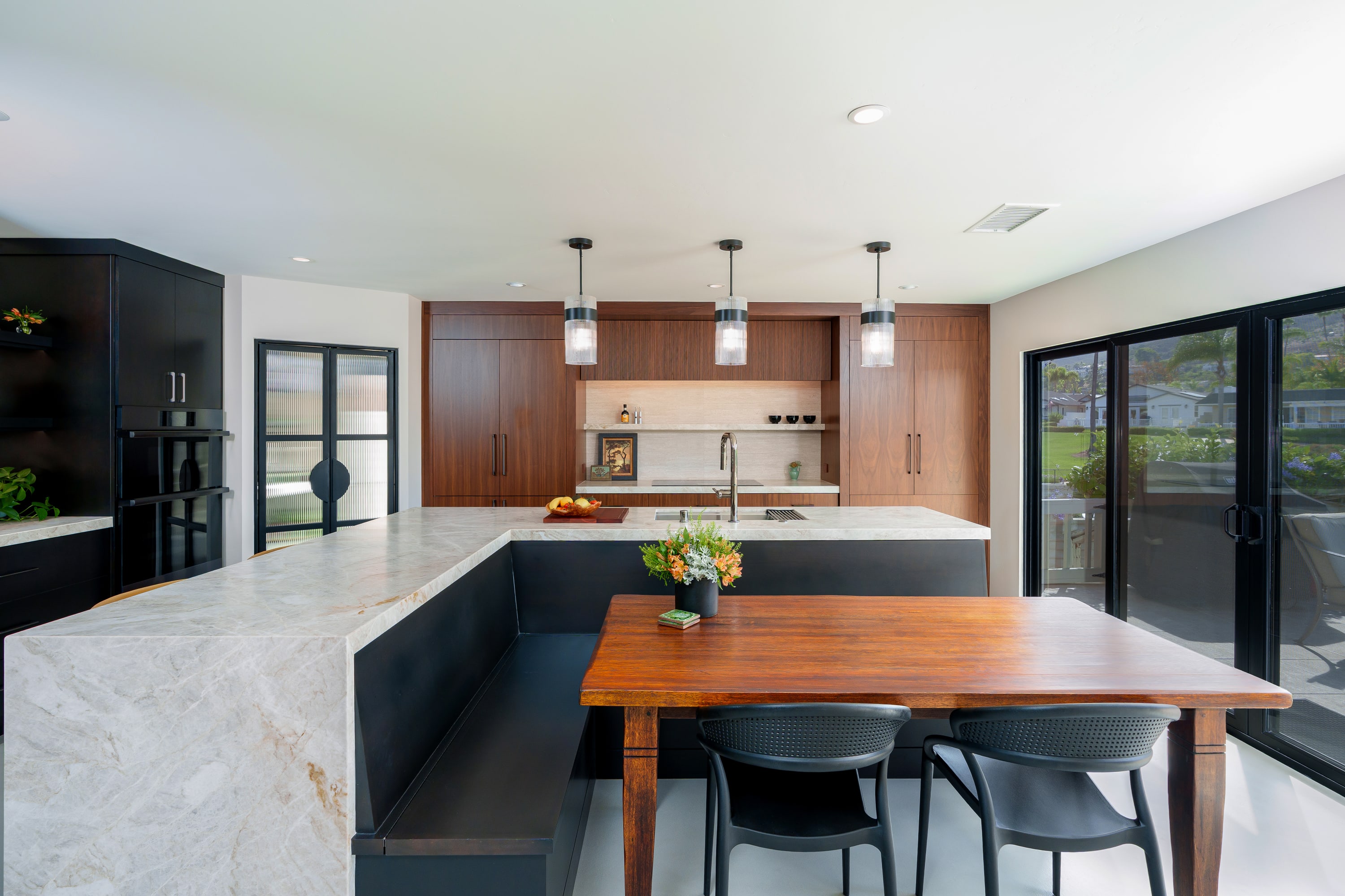 Modern kitchen with walnut cabinetry, white stone waterfall island, leather stools, and sliding doors to a waterfront deck.