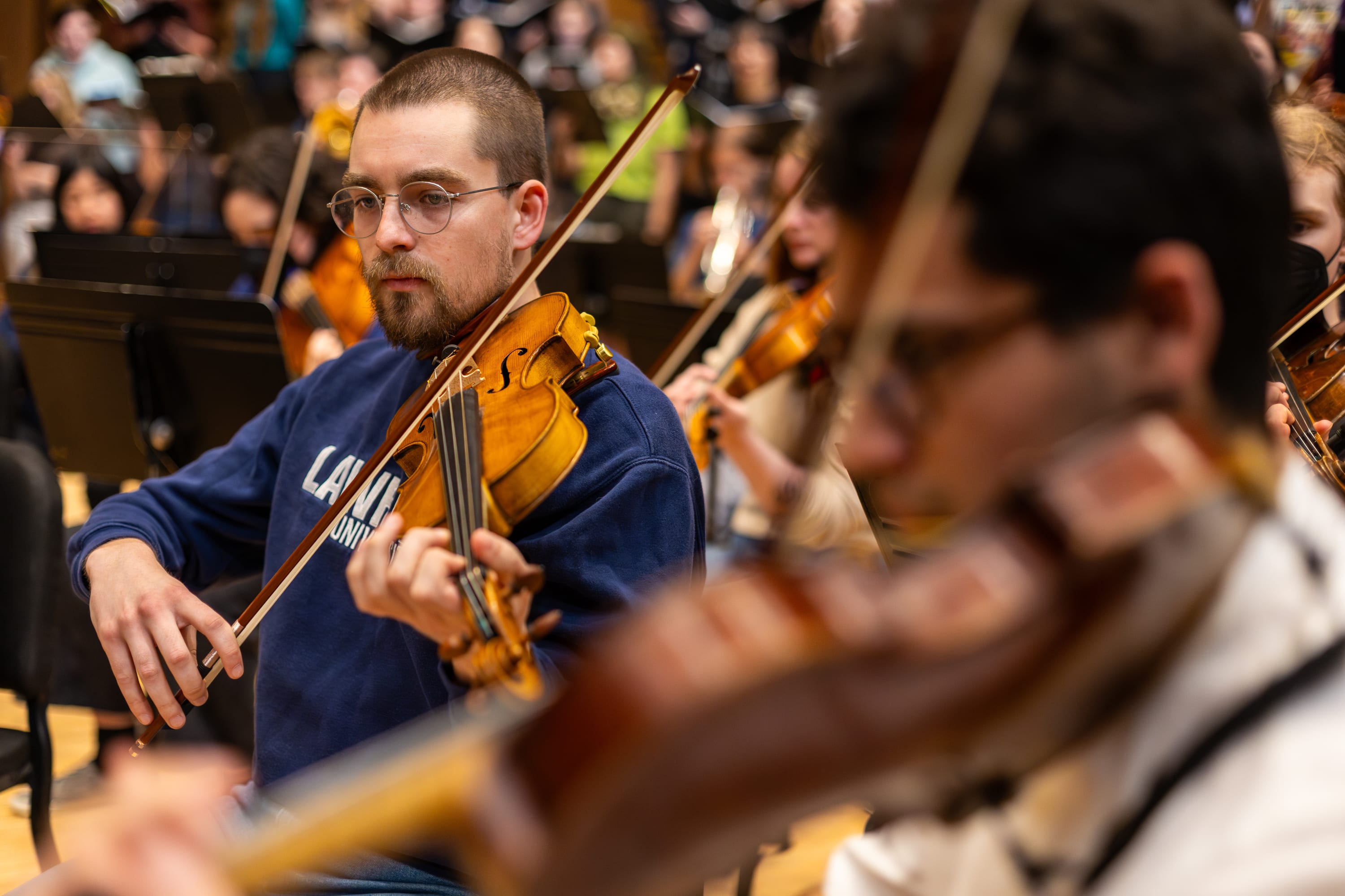 A violinist in a blue Lawrence University sweatshirt plays during an orchestra rehearsal.