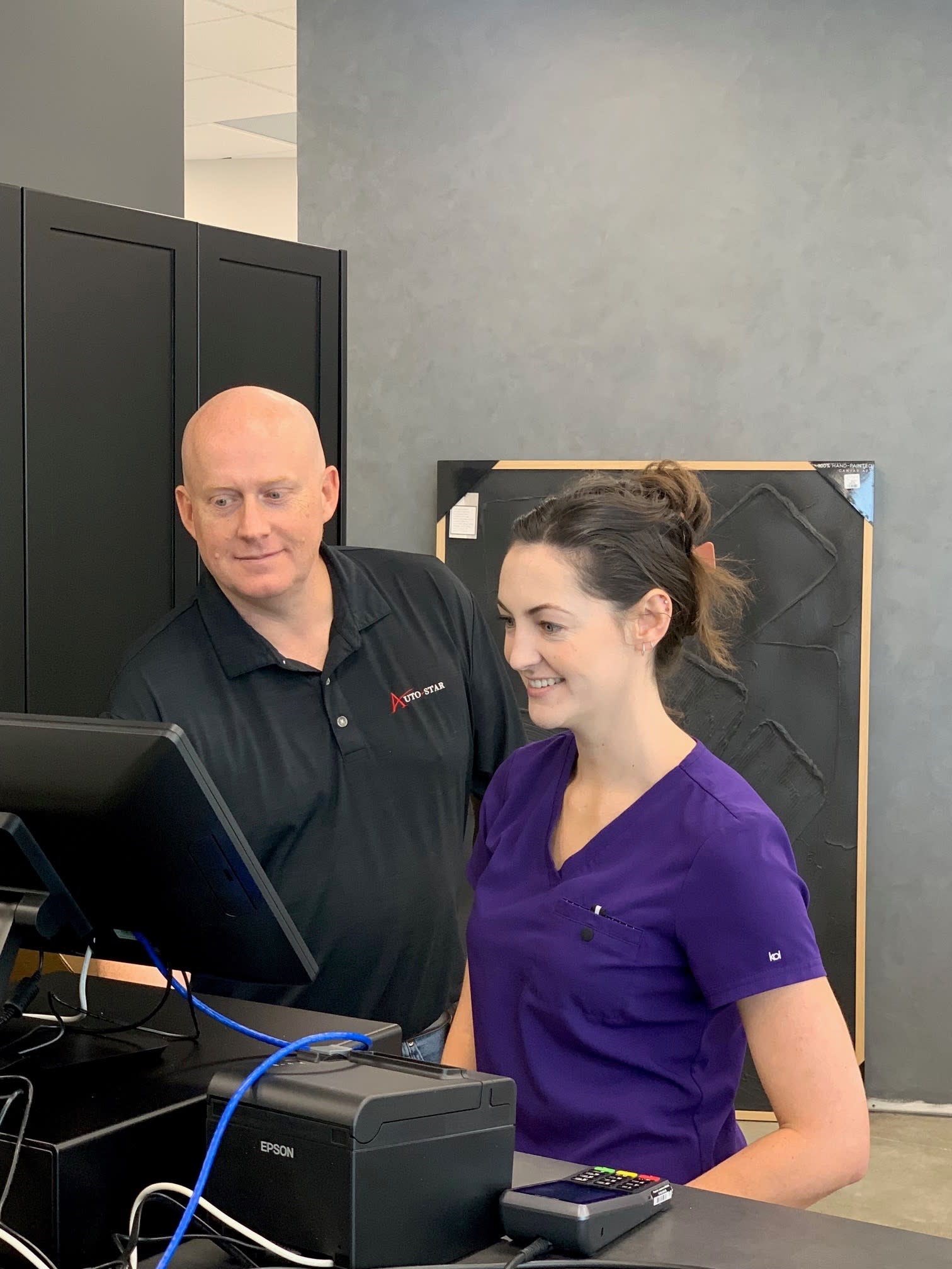 Auto-Star team member assisting a healthcare professional with POS software training at a checkout workstation.