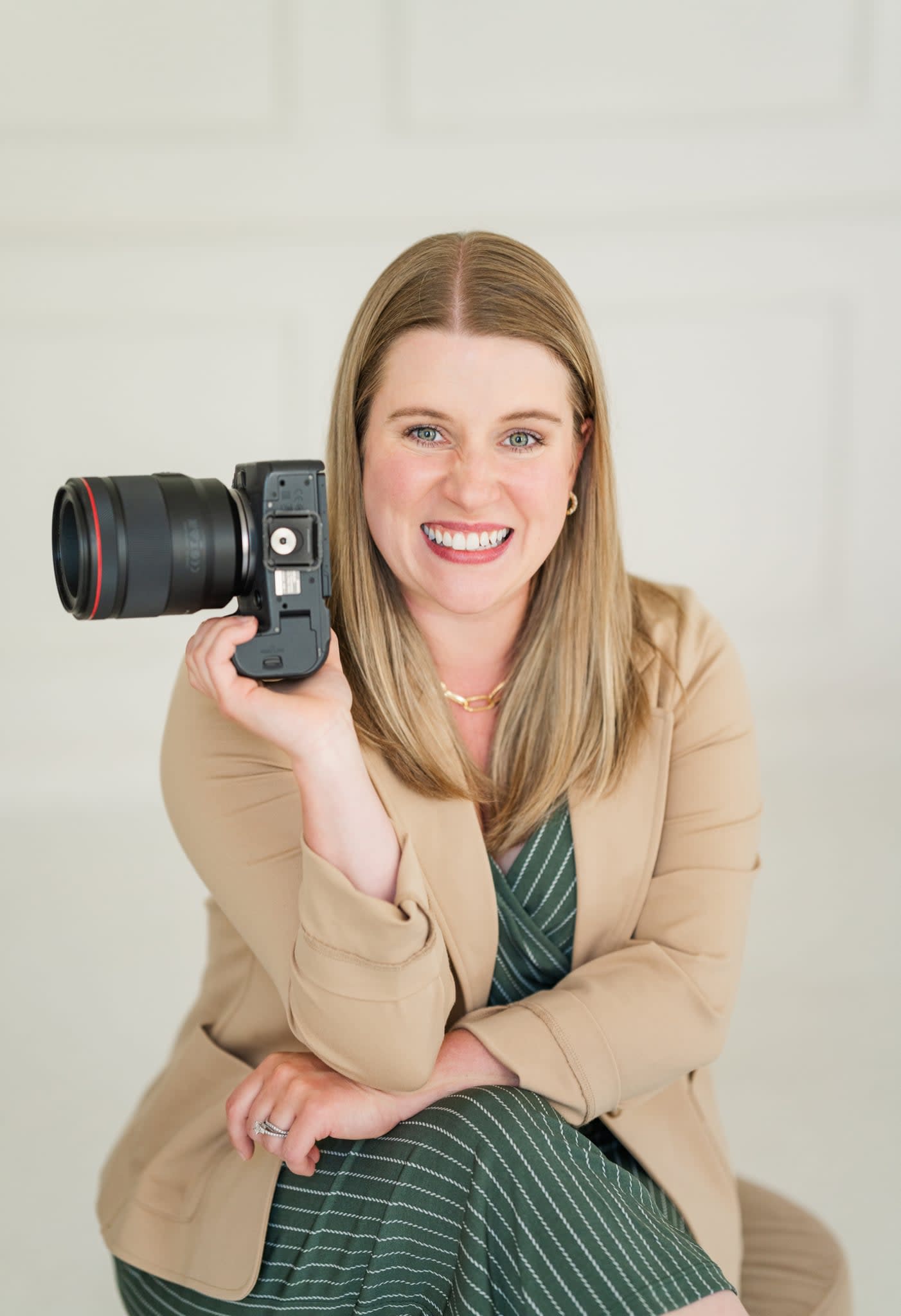 Asha Leena, a family and lifestyle photographer based in Grand Haven, Michigan, smiling while holding a professional camera.