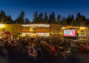 people sitting outside viewing a film with Pine trees on the horizon, around dusk
