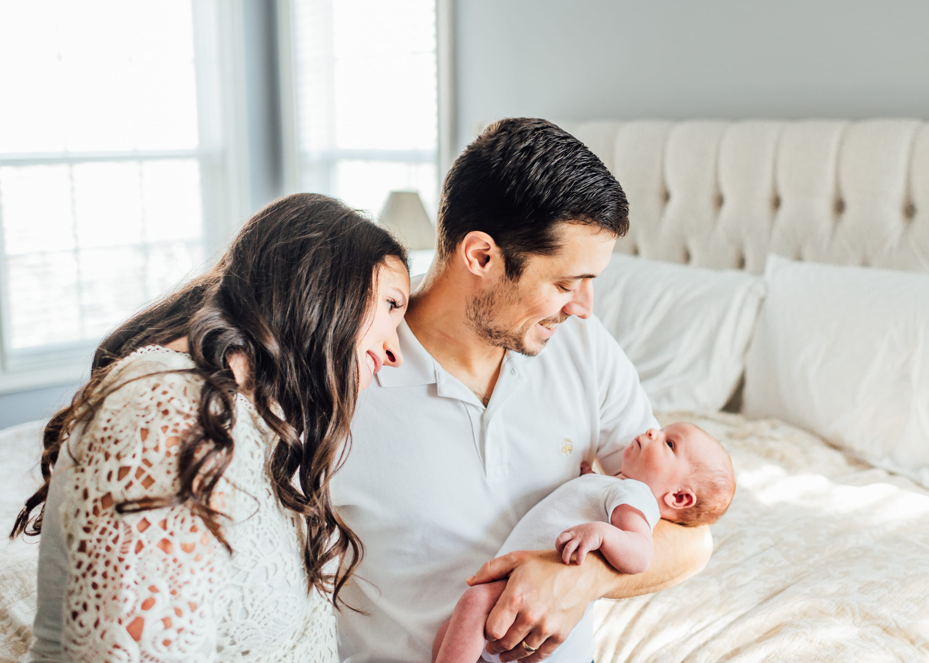 Parents admiring their newborn baby while sitting together on a bed during an in-home lifestyle newborn session.