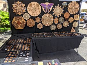 LaserTrees vendor setup with laser cut wood pendants and wall hangings in patterns, such as a butterfly and flower of life