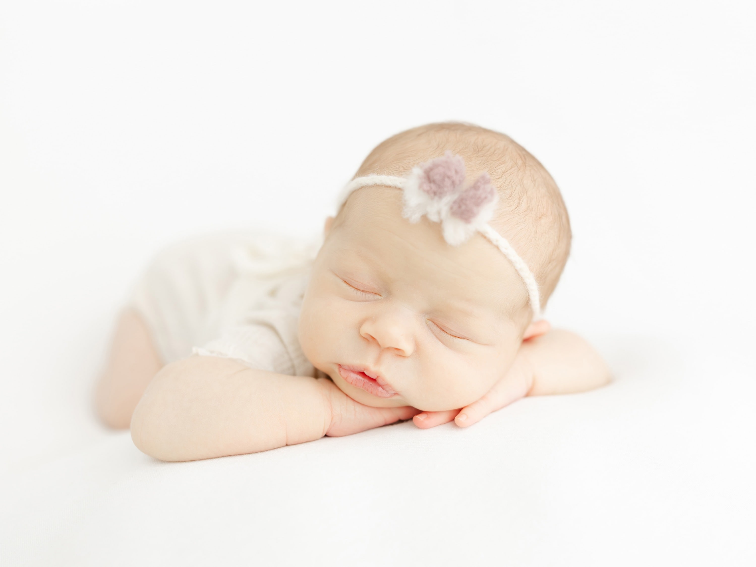 Sleeping newborn baby girl resting on her hands, wearing a soft headband with delicate flowers during a light and airy newbor