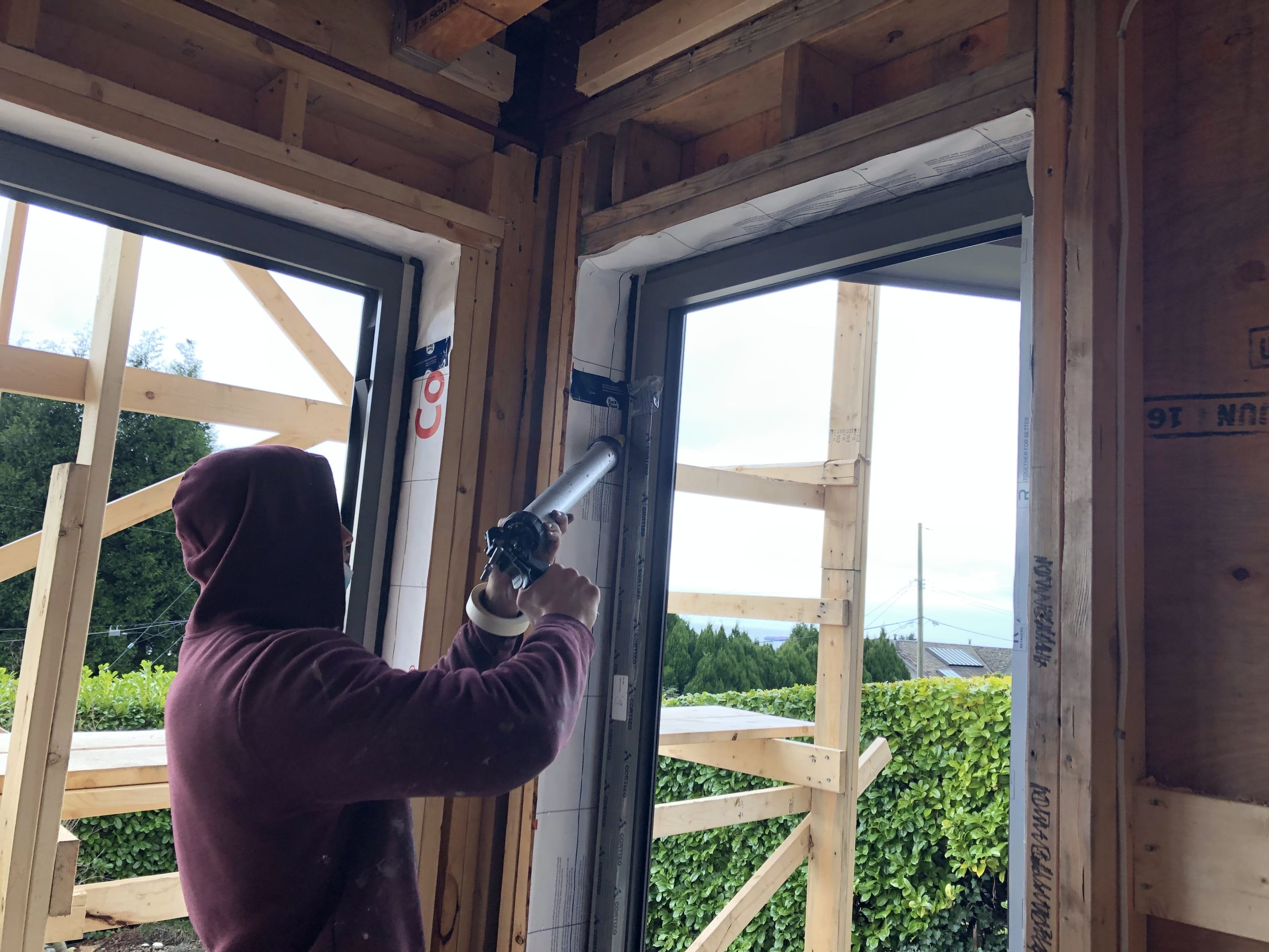 Worker applying sealant around a window frame in a wood‑framed building under construction