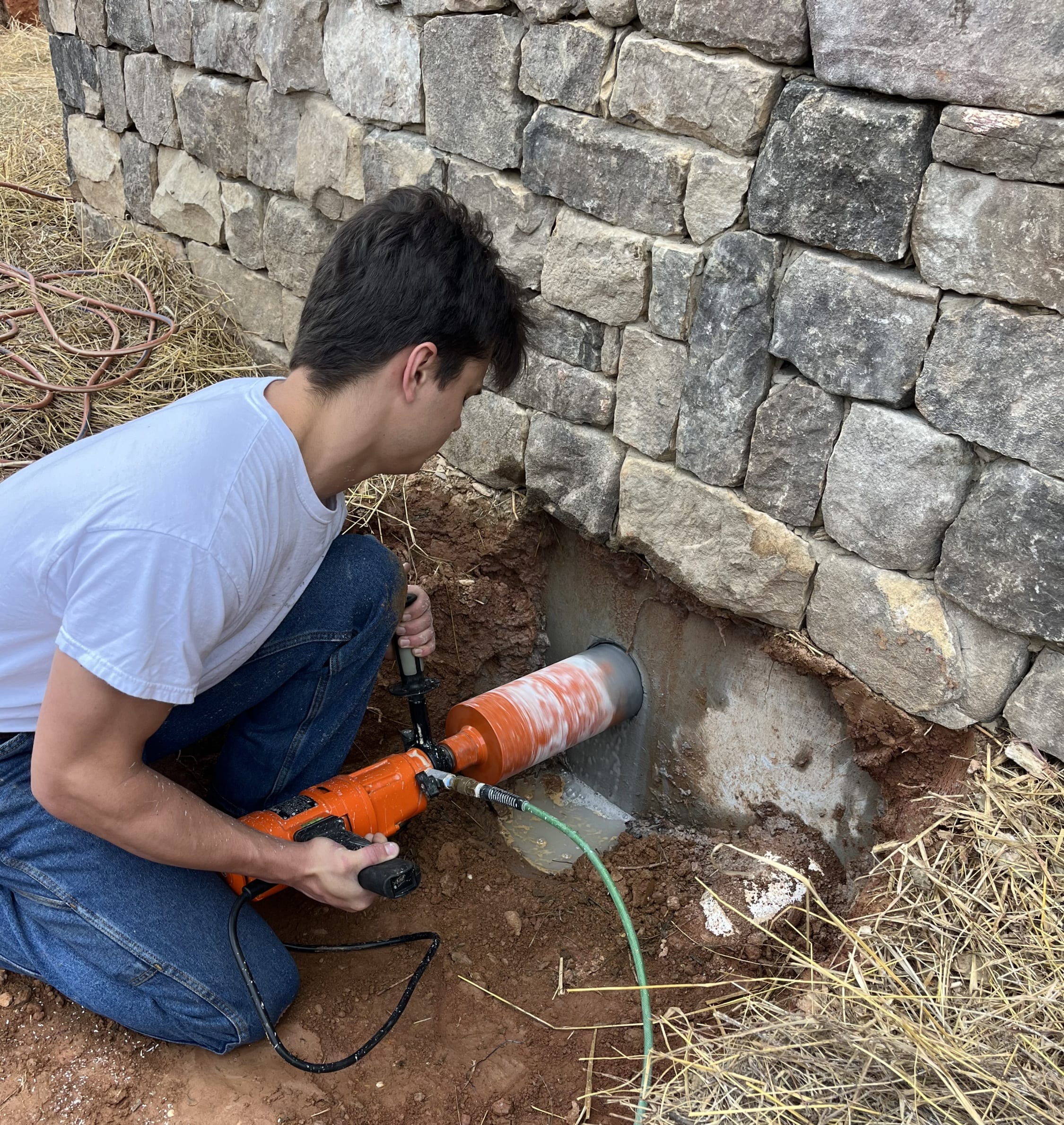 Carver Plumbing team member core drilling through a concrete foundation wall to create an opening for plumbing installation.