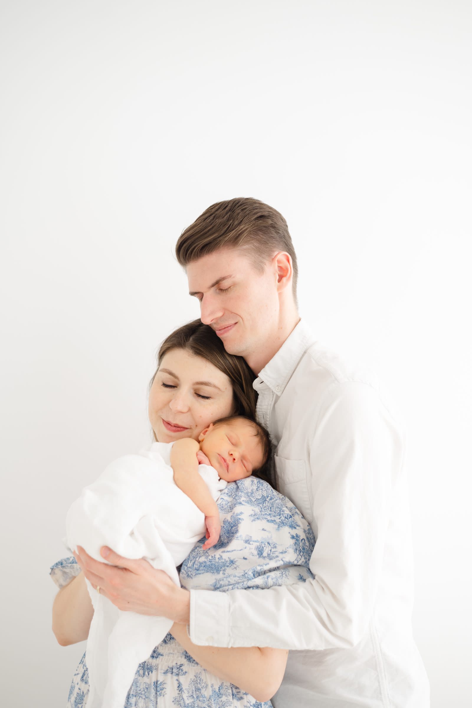 Parents embracing in a bright white studio while mom cradles their newborn