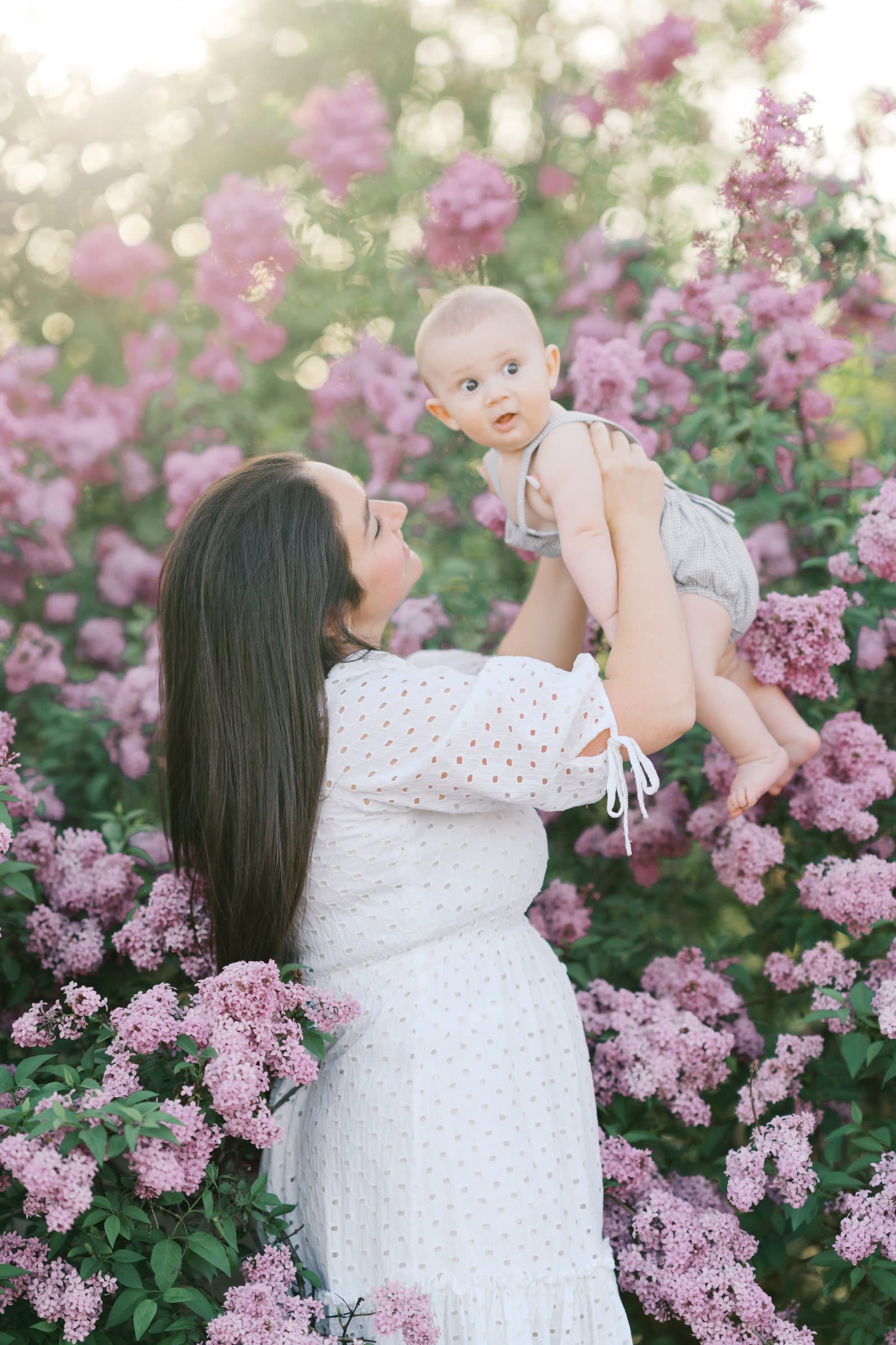 Mother lifting her smiling baby among blooming lilacs