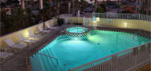 Illuminated pool with hot tub at dusk surrounded by patio chairs and fencing