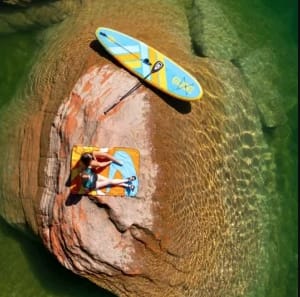 Glide Paddle Sports- two people relaxing on top of a rock surrounded by water with a paddle board