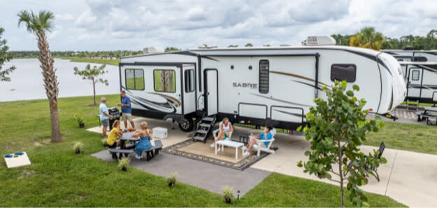 Group sitting at picnic table outside Sabre fifth-wheel trailer near lake