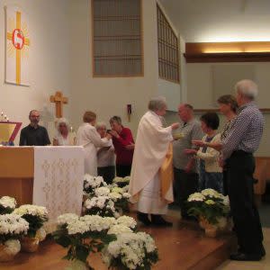 Priest interacting with people in a church with cross and alter and flowers
