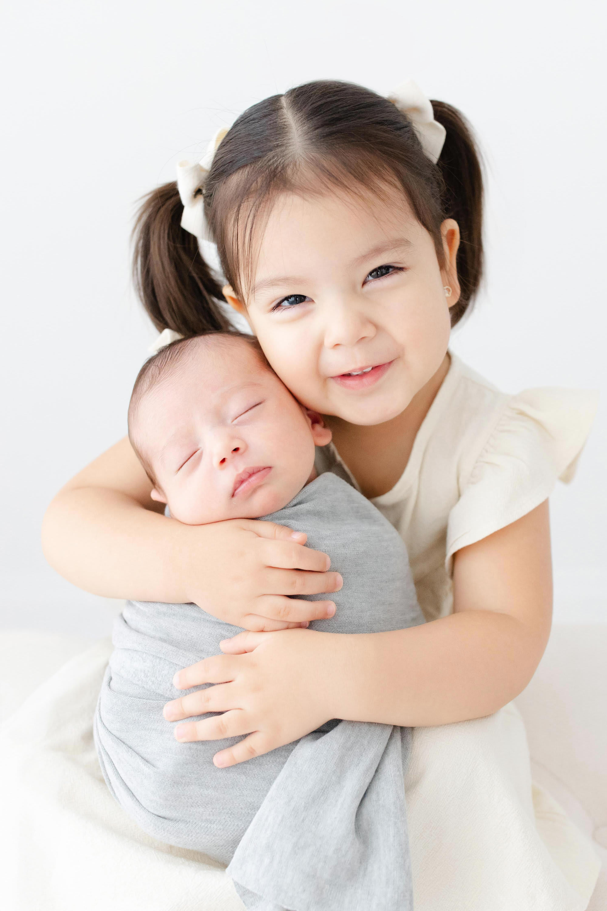 Smiling newborn baby wrapped in a soft white blanket, resting beside a stuffed bunny during a light and airy newborn photogra