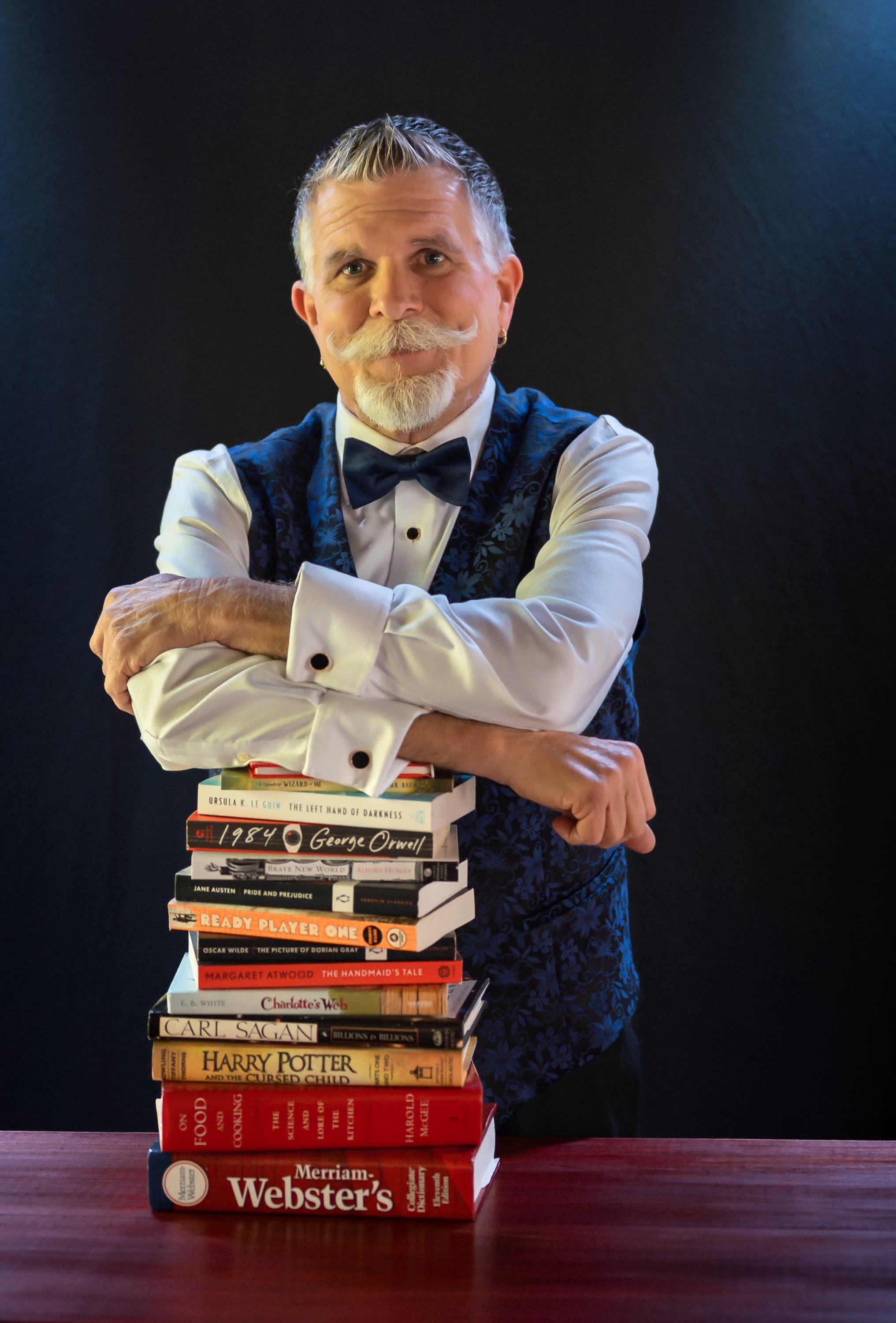 man in a blue vest leaning on a tall stack of books
