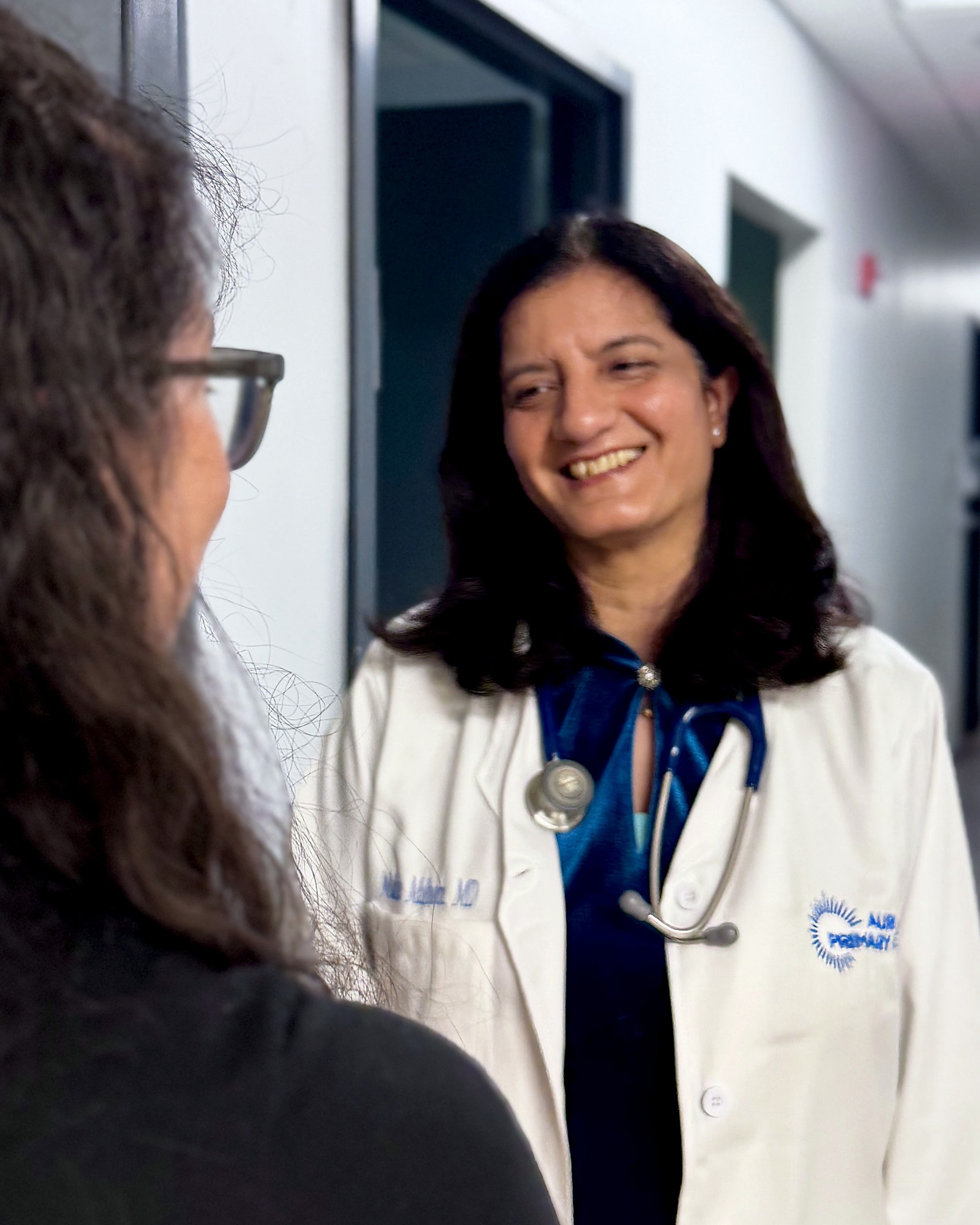 Dr. Mudita Malhotra smiling and greeting a patient in the Aurora Primary Care hallway