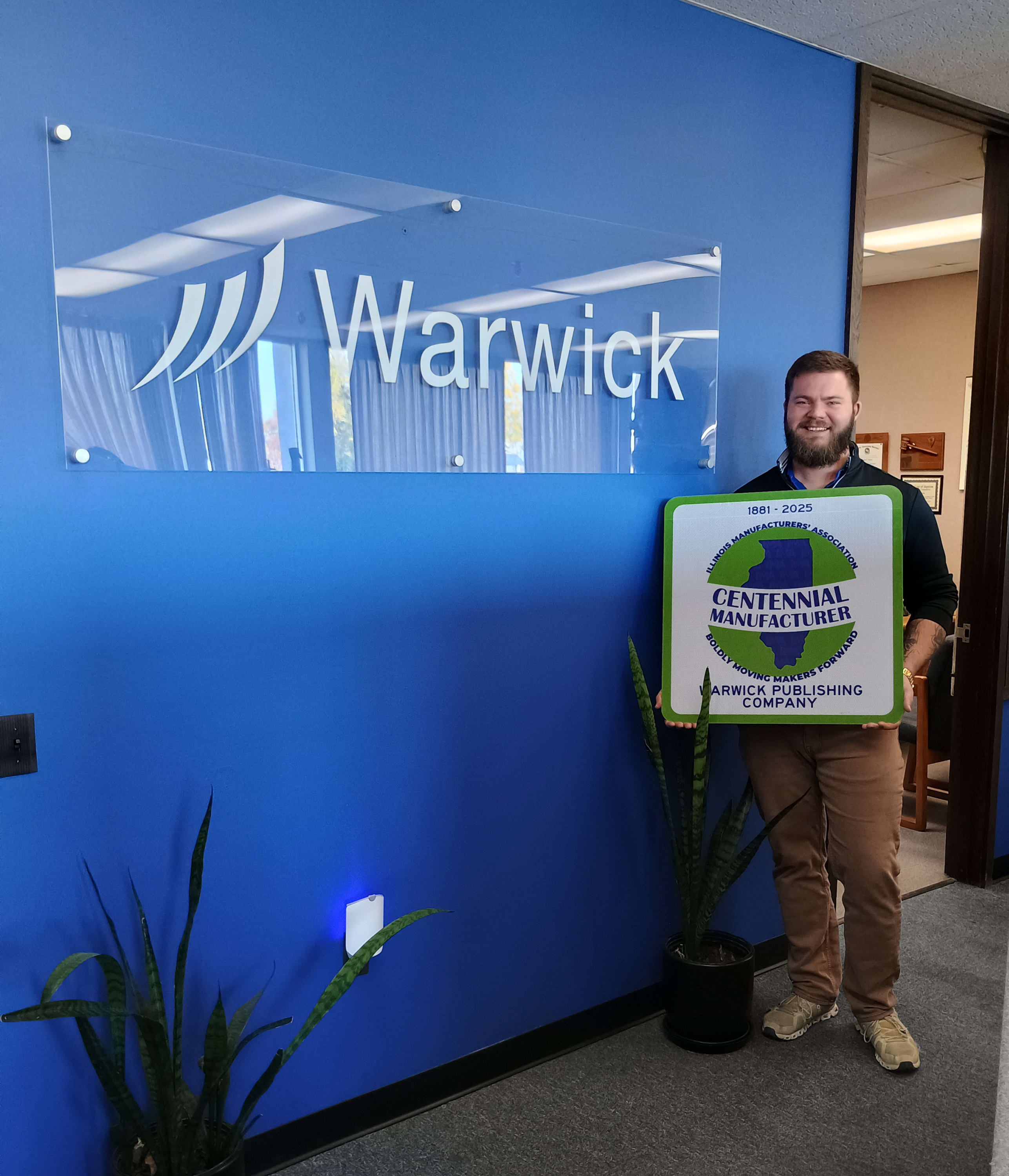 Alex holds a centennial manufacturer sign in Warwick's office