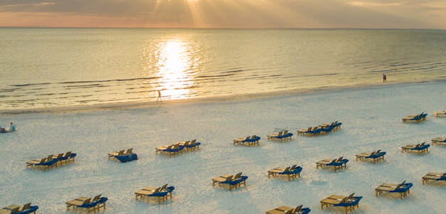 Aerial view of beach at sunset with rows of lounge chairs on white sand
