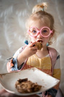 Child enjoying a soft, gluten-free cookie, holding a plate of freshly baked treat