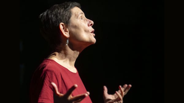 an actor in a red shirt looking up at the sky with hands raised