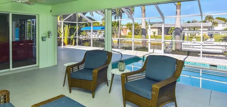 Screened lanai with blue cushioned wicker chairs beside pool overlooking canal