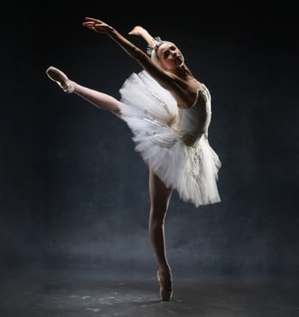 Ballerina wearing an elegant white tutu and headpiece posing in arabesque en pointe