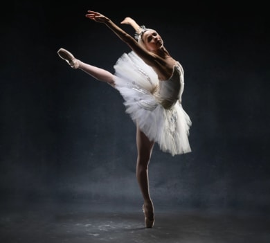 Ballerina wearing an elegant white tutu and headpiece posing in arabesque en pointe