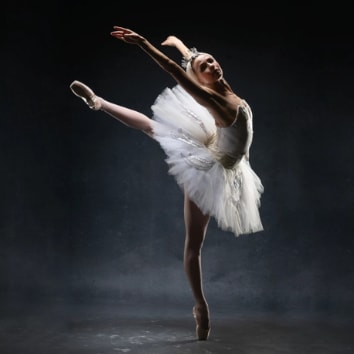 Ballerina wearing an elegant white tutu and headpiece posing in arabesque en pointe