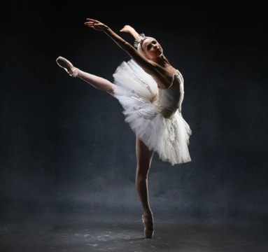 Ballerina wearing an elegant white tutu and headpiece posing in arabesque en pointe