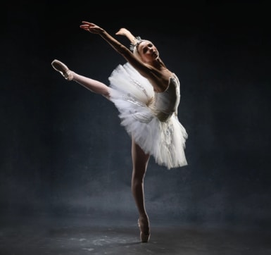 Ballerina wearing an elegant white tutu and headpiece posing in arabesque en pointe