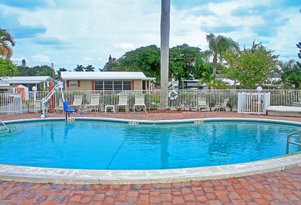 Resort swimming pool with brick deck, lounge chairs, and surrounding trees on sunny day