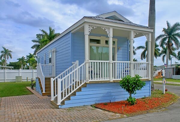 Light blue cottage with white porch railing, staircase, and landscaped front yard
