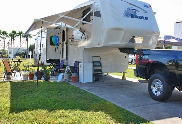 White Eagle fifth wheel RV with awning extended, outdoor chairs, and pickup truck